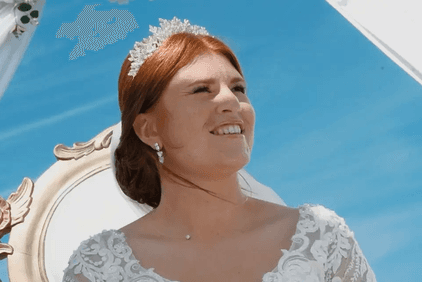Gros plan sur une mariée rousse souriante, coiffée d'un diadème, sous un ciel bleu