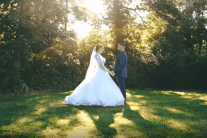 Un couple de mariés se tient face à face, main dans la main, dans une clairière ensoleillée
